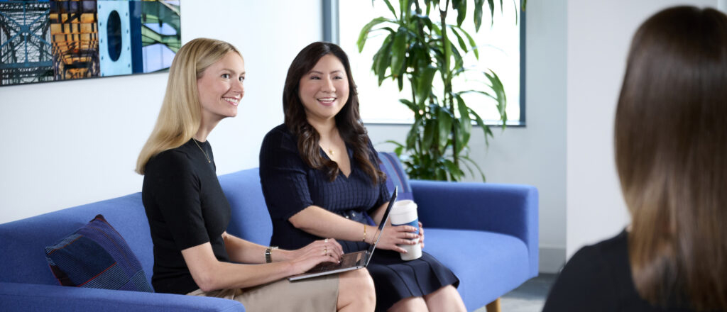 two women sitting on a couch smiling at another woman