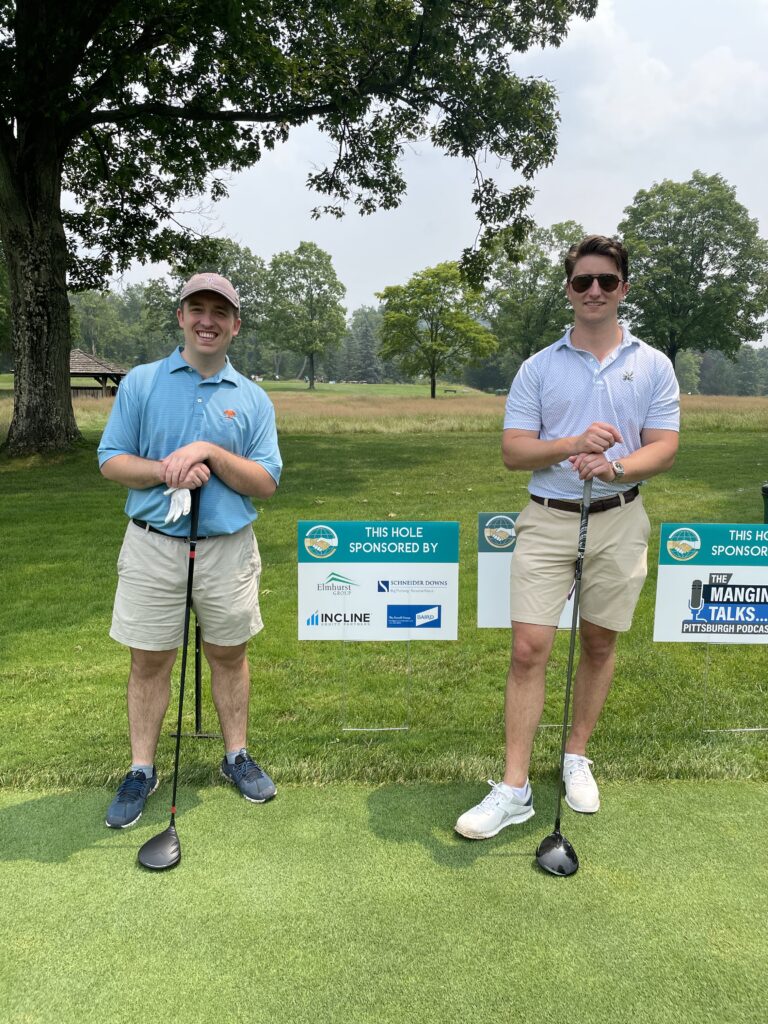 Two men smiling for a photo with there hands on top of a club